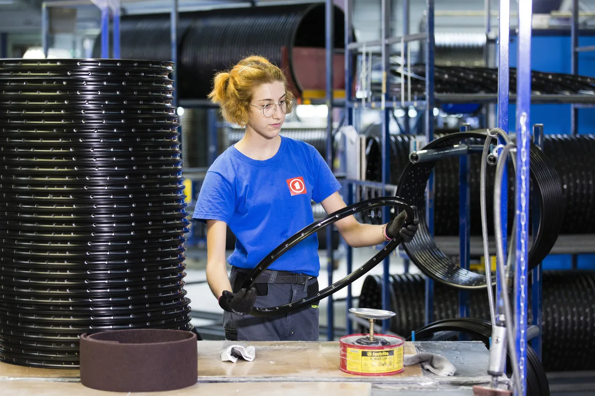 Opératrice Mach1 tenant une jante noire finie devant les piles de l'atelier
